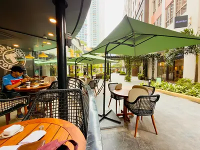 a man sitting at a restaurant with tables and umbrellas at Chic Eastwood City Studio w Pool and Gym Access in Manila
