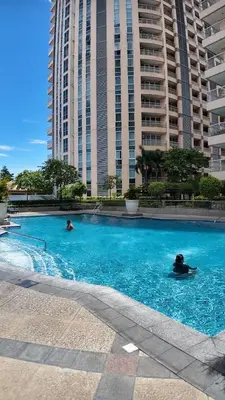two people swimming in a large swimming pool with tall buildings at Venice Luxe Cozy 1 BedRoom, Pool, Netflix, Kitchen, Canal Mall Access in Manila