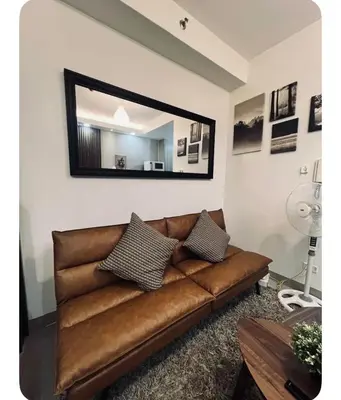 a brown leather couch in a living room with a mirror at Staycay at SRESIDENCES in Manila