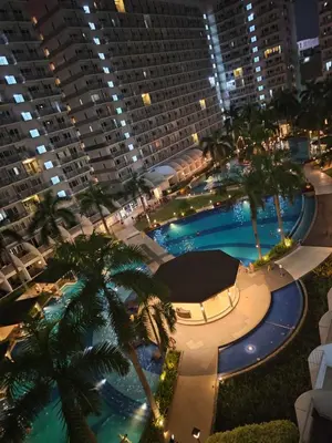 a large pool with palm trees and a large building at Cozy 1BR Balcony Pool View with WiFi & Netflix near MOA and NAIA Airport in Manila