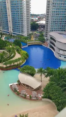 a large swimming pool in a city with tall buildings at Azure Resort Condo with Man-Made Beach Pool in Manila