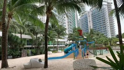 a playground on a beach with palm trees and buildings at Azure Resort Condo with Man-Made Beach Pool in Manila