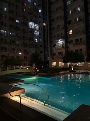 a large swimming pool at night with tall buildings at Cozy City Escape - Jazz Residences in Manila