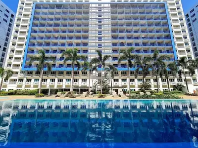 a large building with palm trees in front of a swimming pool at Staycation in Pasay in Manila