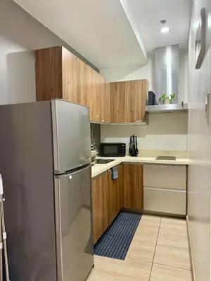 a small kitchen with wooden cabinets and a refrigerator at The Gramercy Residences in Manila