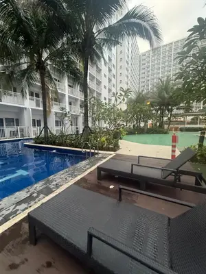 a swimming pool with benches and palm trees and a building at Chen Staycation at Shore in Manila