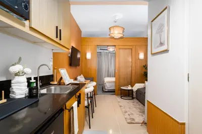 a kitchen with a sink and a living room at Brand New Japandi - Modern 1 BR Walk to MOA in Manila