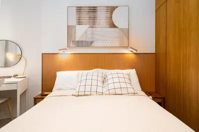 a bedroom with a white bed with a wooden headboard at Brand New Japandi - Modern 1 BR Walk to MOA in Manila