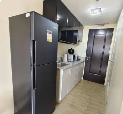 a kitchen with a black refrigerator and white cabinets at NestAway Condo in Manila