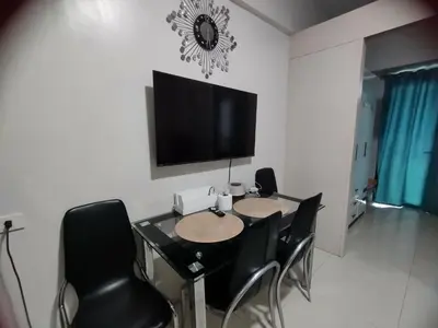a dining room table with black chairs and a flat screen tv at Sea Residences Staycation by Gladys in Manila