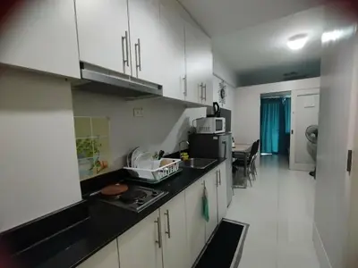 a kitchen with white cabinets and a black counter top at Sea Residences Staycation by Gladys in Manila
