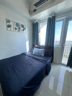 a bedroom with a bed with blue sheets and windows at Jazz Residences Condominium in Manila
