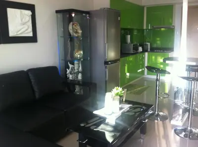 a living room with a black couch and a green kitchen at Sea Residences - Rheiyn in Manila