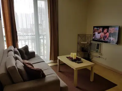 a living room with a couch and a table and a tv at ORTIGAS 2 Br Corner Unit With 2 Queen Across Shangrila in Manila