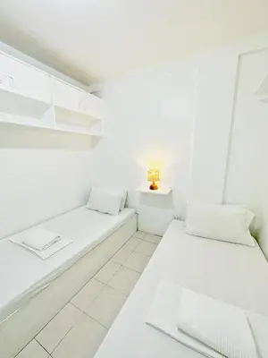 two beds in a white room with a lamp at Nomads MNL Backpackers Homestay - near Airport in Manila