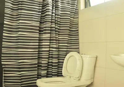 a bathroom with a toilet with a black and white shower curtain at Food District Hostel - Ortigas Kapitolyo in Manila