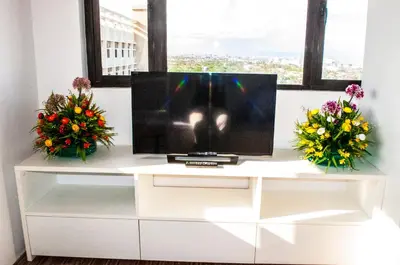 a television on a white cabinet with flowers on it at Titan Condo at Studio City Tower 1 Alabang in Manila