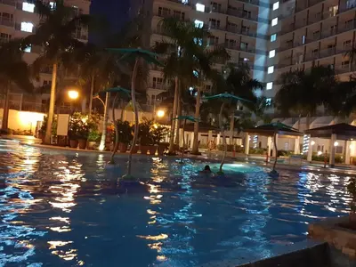 a swimming pool at night with palm trees and buildings at The Palawanos Home at Shell Residences in Manila