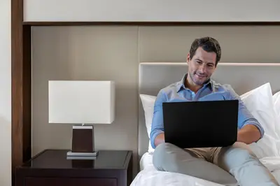 a man sitting on a bed with a laptop at Manila Marriott Hotel at Newport World Resorts in Manila