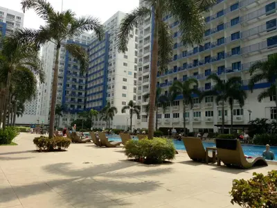 a row of chairs in a courtyard with palm trees and buildings at Chin's Place Sea Residences MOA in Manila