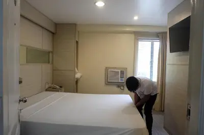 a woman standing next to a large bed in a room at Spaces Hotel Makati in Manila