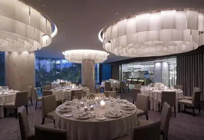 a dining room with tables and chairs and chandeliers at New World Makati Hotel, Manila in Manila