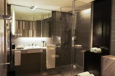 a bathroom with a shower with a sink and a mirror at New World Makati Hotel, Manila in Manila