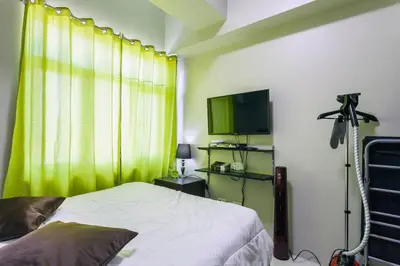 a bedroom with a bed with a green curtain and a television at Yong's Place at Vista Residences Taft in Manila
