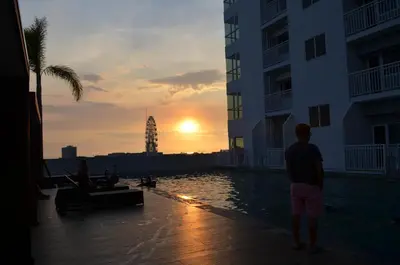 a man standing next to a pool with the sunset at Jovic's Condo at Breeze Residences. in Manila
