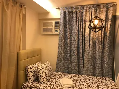 a bedroom with a bed and a curtain and a lamp at Grand Apartment near BGC in Manila