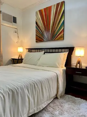 a bedroom with a large white bed with two lamps at East Ortigas Mansions by MA in Manila