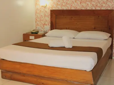a bedroom with a large wooden bed with white sheets at Rosas Garden Hotel in Manila