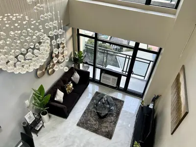 a living room with a black couch and a chandelier at 2-story Penthouse with 5 Balconies in Manila
