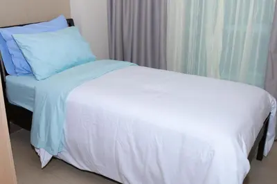 a white bed with blue pillows next to a window at De Luxe 7QRS in Manila