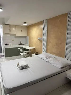 a bedroom with a large white bed and a kitchen at Frank Lloyd Apartelle in Manila