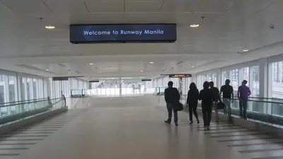 a group of people walking down a hallway in an airport at One Palm Tree Villas in Manila