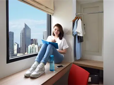 a girl sitting on a desk reading a book in a hotel room at Hop Inn Hotel Alabang Manila in Manila