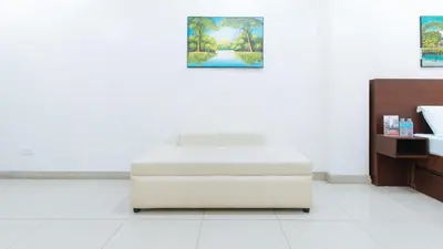 a white ottoman in a white room with paintings on the wall at RedDoorz near Pasay Taft in Manila