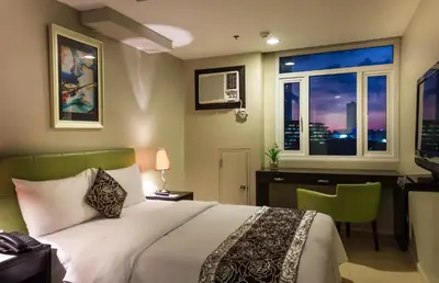 a bedroom with a bed and a desk and a window at The Exchange Regency Residence Hotel Managed by HII in Manila