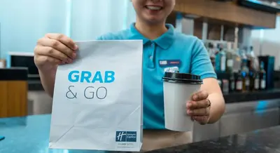 a man is holding a cup of coffee and a sign at Holiday Inn Express Manila Newport City by IHG in Manila