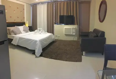 a bedroom with a bed and a tv and a chair at H&M One Palmtree Villas in Manila