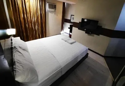 a bedroom with a white bed and a television at Lorenzzo Suites Hotel Makati in Manila