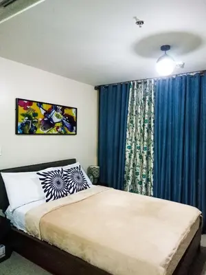 a bedroom with a bed and a window with blue curtains at Uptown Mall Area Fort Bonifacio Manila in Manila