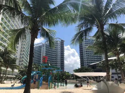a playground on a beach with palm trees and buildings at AZURE URBAN RESORT RESIDENCE R&C - Parañaque in Manila