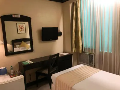 a hotel room with a bed and a desk and a mirror at Tower Inn Makati Business Hotel in Manila