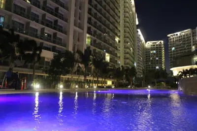 a large pool with blue lights in a city at night at AZURE C4 BEACHPOOL balcony wifi MULTIPLE UNITS in Manila