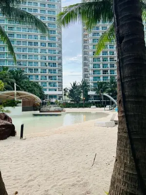 a beach with a palm tree and tall buildings at Azure Urban Resort Residences, Condo, Manila Airport, Wave-Pool, Tropical Vibe in Manila