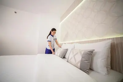 a woman standing next to a bed with white pillows at The Charter House in Manila