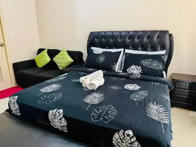 a bed with a black headboard and pillows and a couch at One Palm Tree Villas across NAIA-T3 in Manila