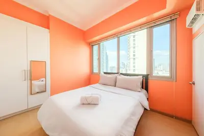 a large white bed in a room with orange walls at StayHere Burgos Circle 1 Bedroom Avant@Fort Gym in Manila